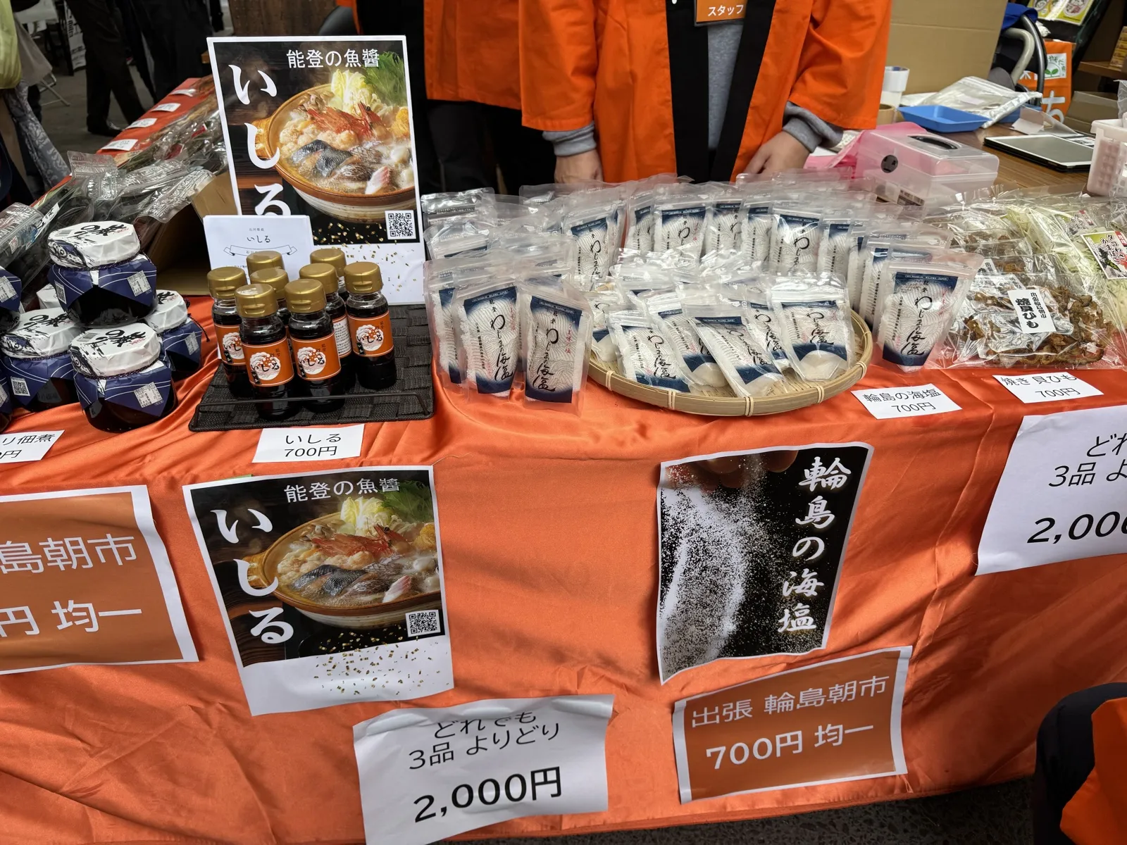 オレンジの布を掛けた売り台に、塩やいしるの商品が並んでいる